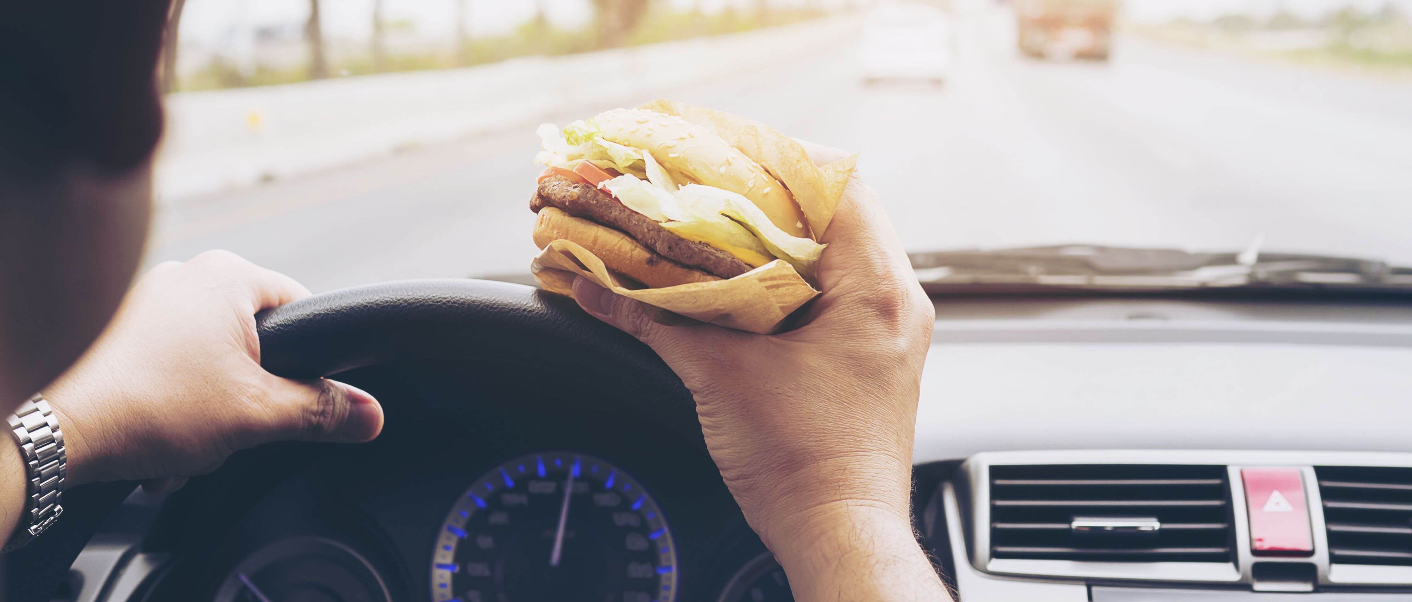 Man eating a hamburger in the car while driving